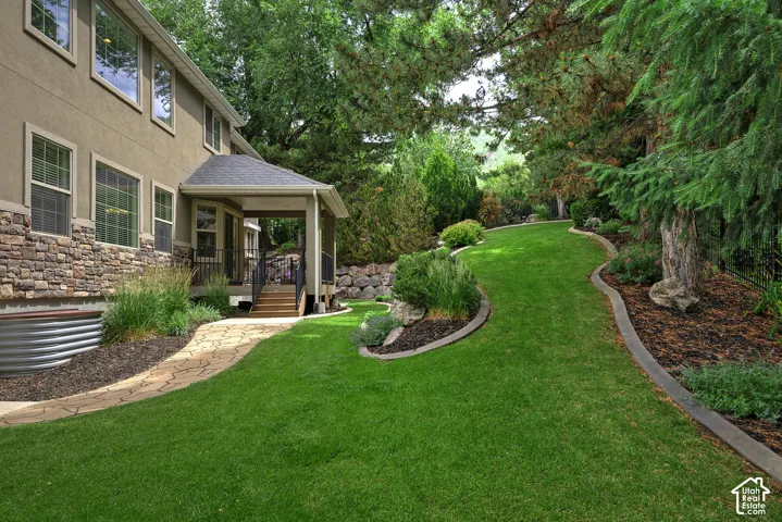 Expansive backyard featuring a meticulously manicured lawn with curved hardscape edging, mature shade trees, and a brick paver patio adjoining the home's covered outdoor living area