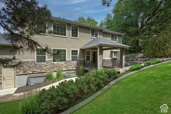 Elegant two-story residence featuring a stucco exterior with stone accents, multiple windows with dark framing, and a covered front porch entry