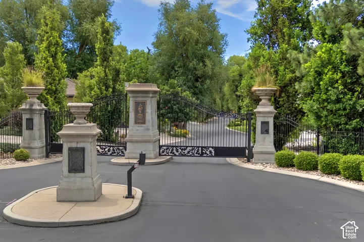 Wrought iron entry gates with decorative scrollwork, flanked by stone pillars and mature landscaping