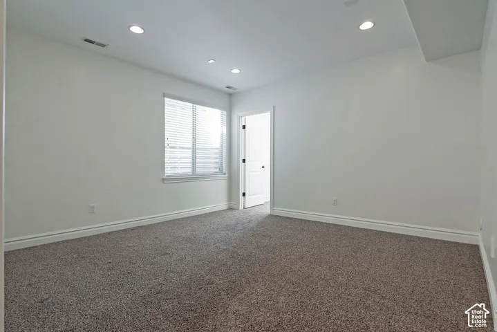 Bright, open bedroom featuring neutral wall finishes, recessed ceiling lighting, carpeted flooring, and a window with plantation shutters