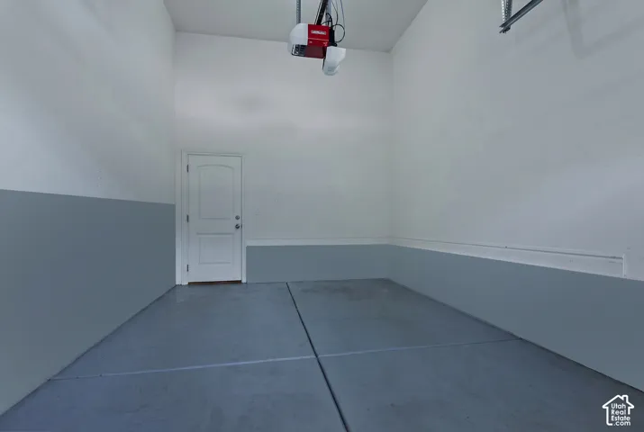 Attached garage with a finished concrete floor, painted interior walls, overhead garage door opener, and a panel door