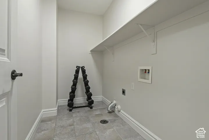 Tiled flooring with a central floor drain, a wall-mounted utility sink connection, and an integrated shelf with support brackets