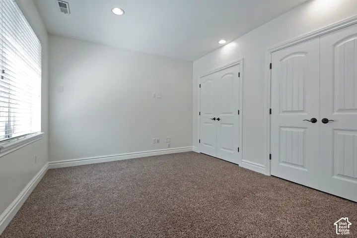 Recessed lighting, white interior walls, white trim, two white paneled doors, and brown carpeting