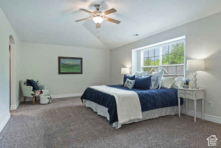 Angled vaulted ceiling, ceiling fan with integrated lighting, recessed window, wall-to-wall carpeting, arched doorway