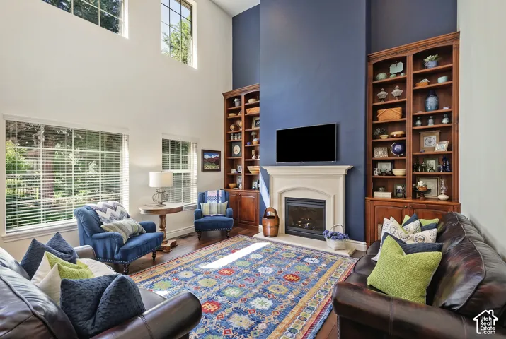 Spacious living area featuring a high ceiling, multiple windows, a stone fireplace, and built-in wood shelving