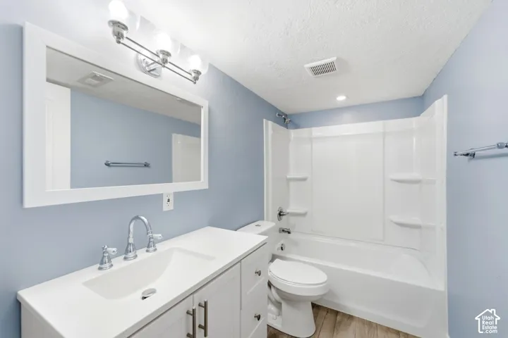 White framed vanity mirror, chrome fixture vanity lighting, integrated vanity sink, wood-finish flooring, and a white fiberglass tub with shower