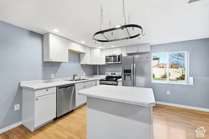 Modern kitchen featuring white cabinetry, stainless steel appliances including a built-in microwave and gas range, quartz countertops, a large center island with seating, wood-finish flooring, and abundant natural light from a corner window
