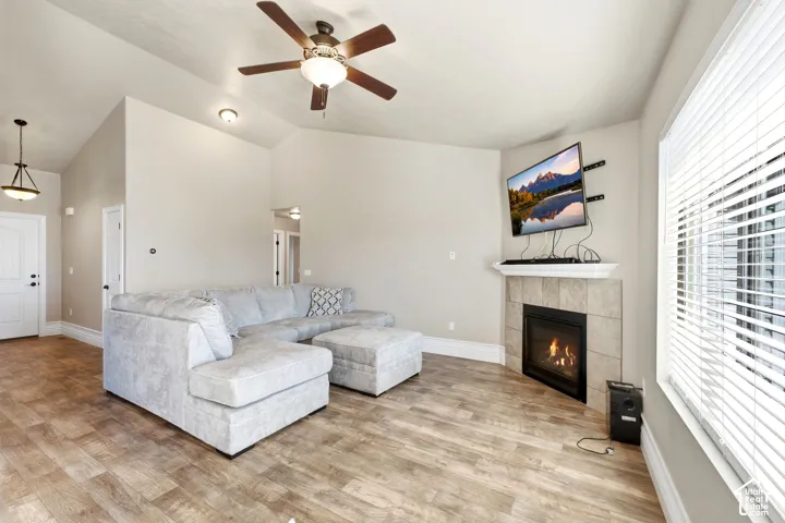 Wood-finish flooring, vaulted ceiling, corner fireplace with a tiled surround, built-in mantel, and ceiling fan with lighting