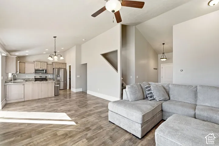 Open-concept living area featuring wood-finish flooring, vaulted ceilings, and a kitchen with light-toned cabinetry and stainless steel appliances