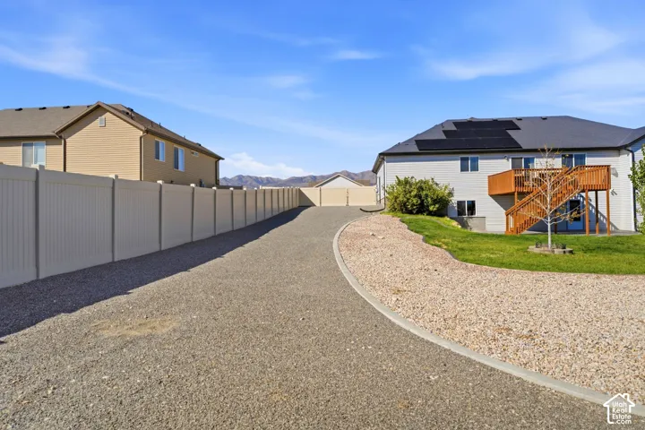 Extended gravel driveway with paved border, private vinyl fencing, and a two-story residence featuring a large deck and solar panels