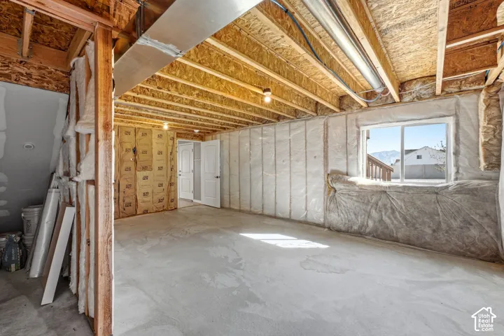 Unfinished basement featuring exposed wood framing, concrete flooring, and an egress window