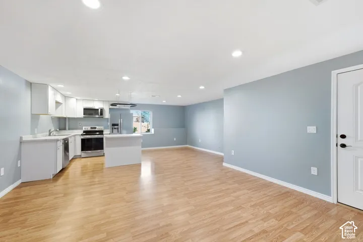Open-concept living area featuring wood-finish flooring, recessed lighting, and a kitchen with white cabinetry