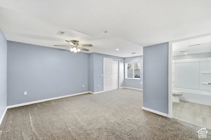 Expansive room with neutral carpeting, light blue walls, and a ceiling fan with integrated lighting