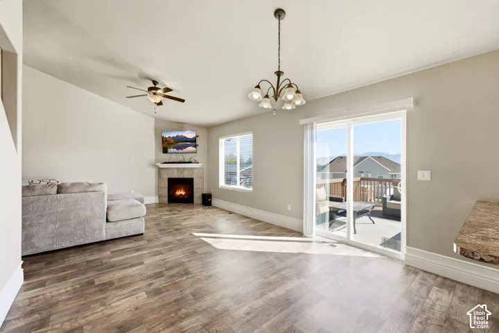 Wood-finish flooring throughout, a tiled corner fireplace, a ceiling fan, and a chandelier
