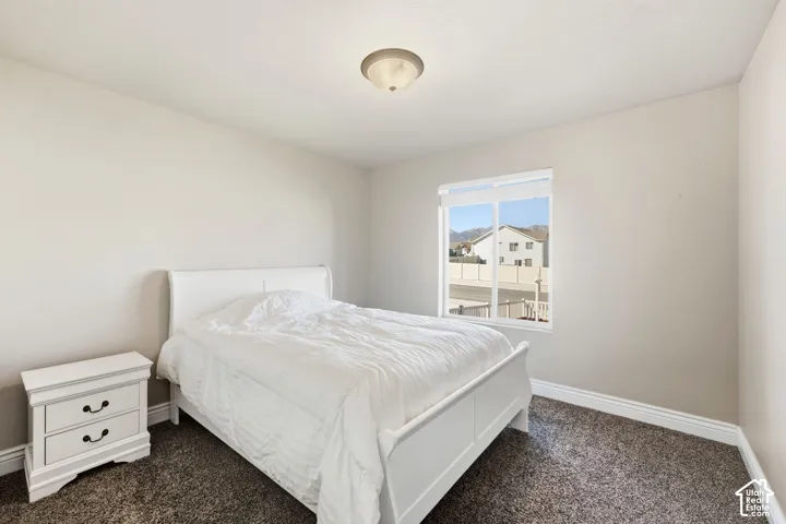 Bright secondary bedroom featuring a carpeted floor, white wooden bed frame, nightstand with drawer storage, and large window with natural light and neighborhood vistas