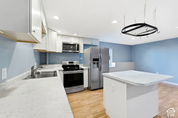 Kitchen featuring white cabinetry, stainless steel appliances, a center island with a light-toned countertop, and wood-finish flooring