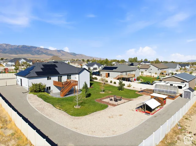 Exterior featuring solar panel array, attached garage, wood-finish deck with stairs, expansive gravel area, and a fenced perimeter