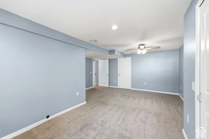 Expansive room featuring light gray walls, plush carpet flooring, a ceiling fan with integrated lighting, and recessed ceiling lights