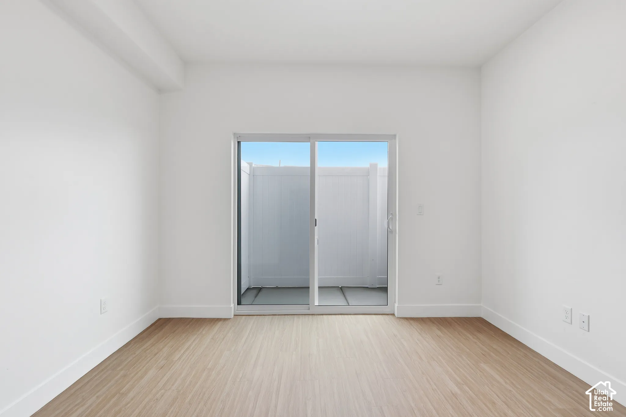Expansive room featuring wood-finish flooring, white painted walls, and a sliding glass door