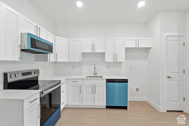 White shaker-style cabinetry, stainless steel range, built-in microwave, light wood-finish flooring, and a dishwasher
