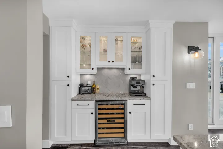 Built-in cabinetry with glass-front uppers, herringbone tile backsplash, integrated wine refrigerator, and stone-finish countertop