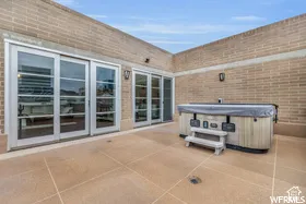 Spacious outdoor patio featuring light-colored pavers, brick walls, and multiple sets of sliding glass doors