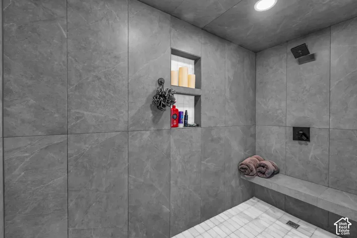 Spacious shower with large format tile, built-in shelving, a shower bench, and dark finish fixtures