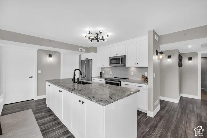 Kitchen featuring white shaker cabinetry, an island with a stone countertop, dark wood-finish flooring, and stainless steel appliances