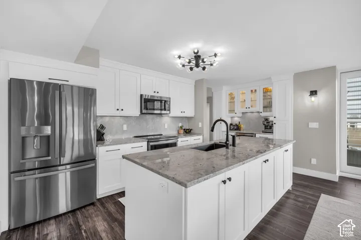 Kitchen featuring white shaker-style cabinetry, a large kitchen island with a dark sink and matte black faucet, stainless steel appliances, and wood-finish flooring