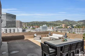 Expansive rooftop deck featuring a combination of concrete and wood-finish flooring, surrounded by a low brick wall, and offering distant mountain scenery