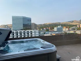Rooftop deck featuring a hot tub, brick privacy wall, and urban landscape with distant mountains