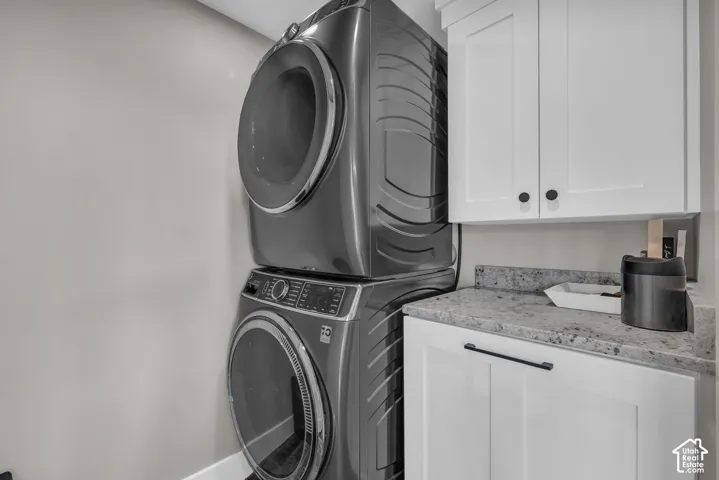 White shaker-style cabinetry with matte black hardware, stacked laundry appliances, and a light-toned countertop