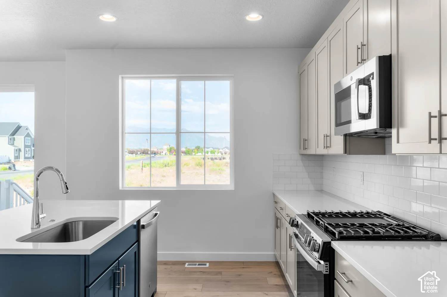 Kitchen featuring light-finish cabinetry, white subway tile backsplash, stainless steel appliances, and a central island with a sink and dark blue base cabinetry