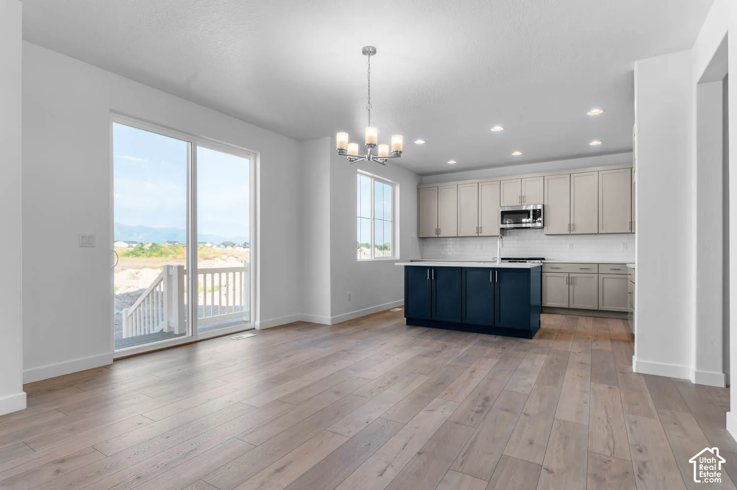 Open-concept living space with wood-finish flooring, a contemporary chandelier, and a kitchen featuring a navy island, light cabinetry, and stainless steel appliances