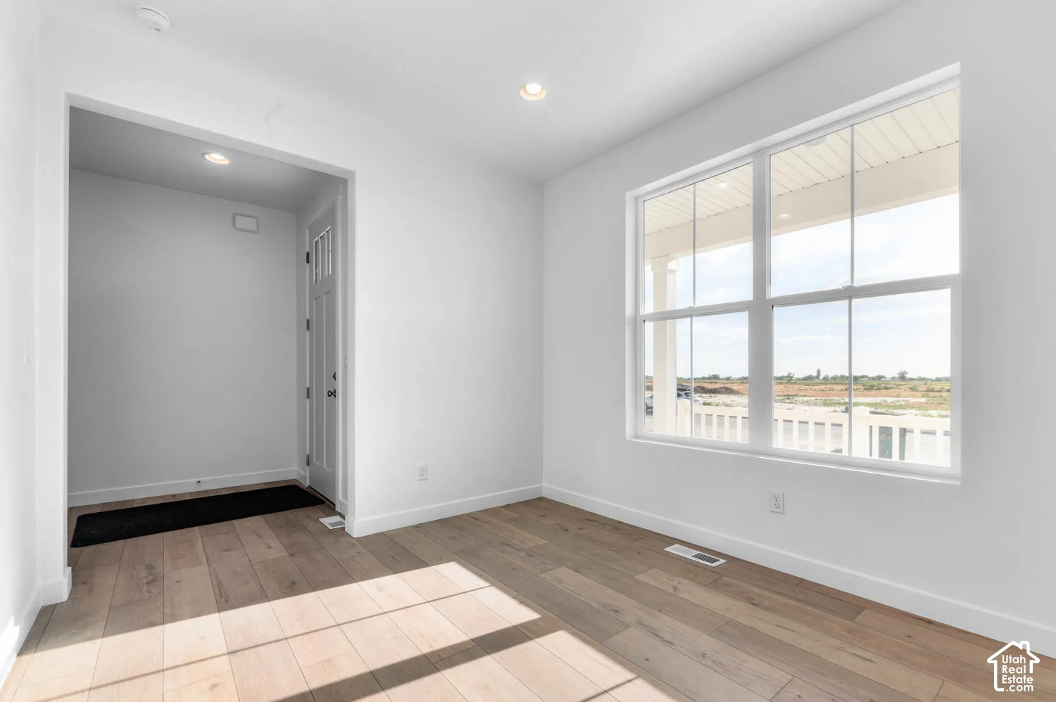 Recessed lighting, wood-finish flooring, white walls, large multi-pane window, and a paneled entry door