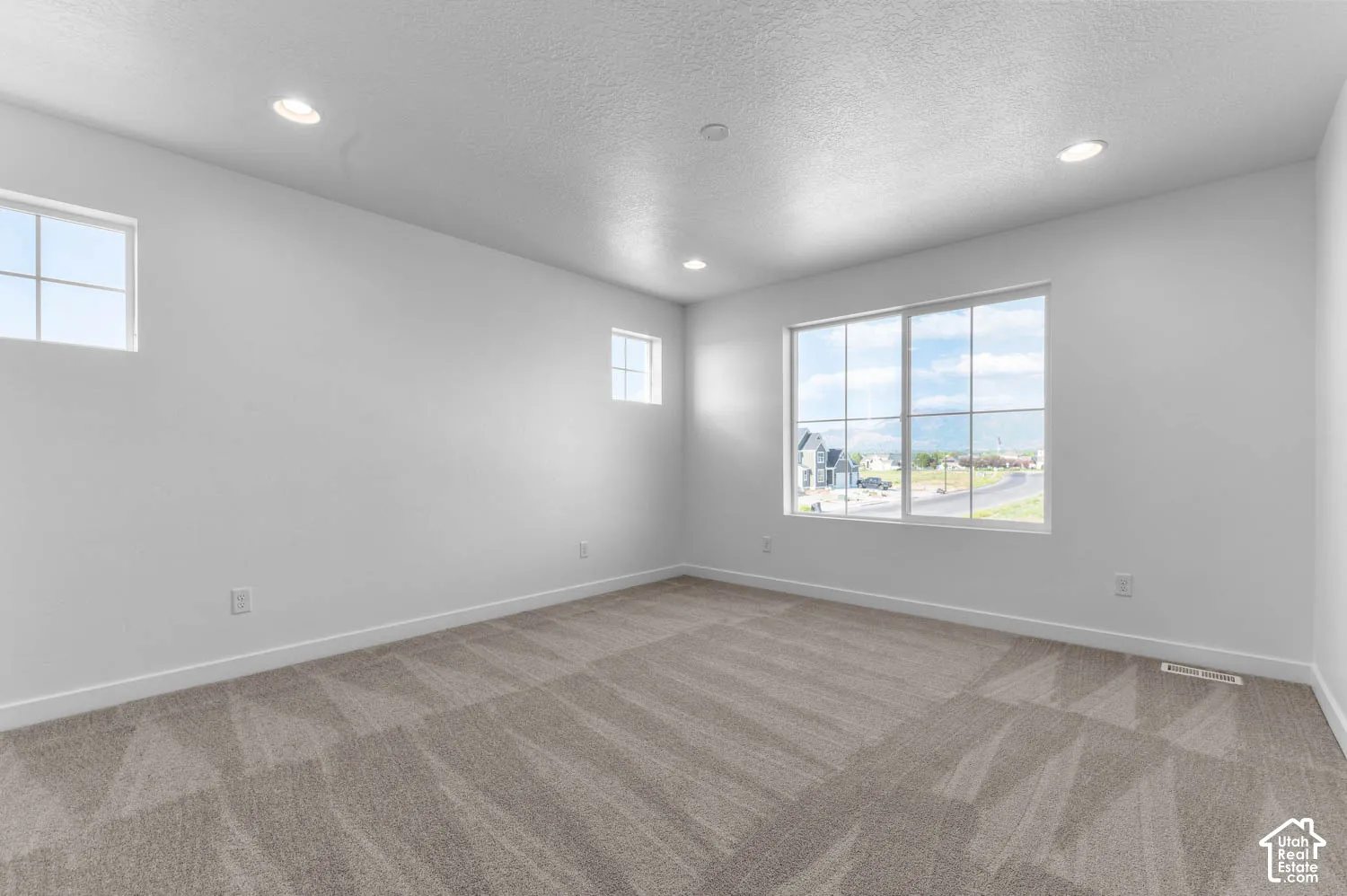 Recessed ceiling lighting, multiple windows, neutral wall color, patterned carpeting, and white trim