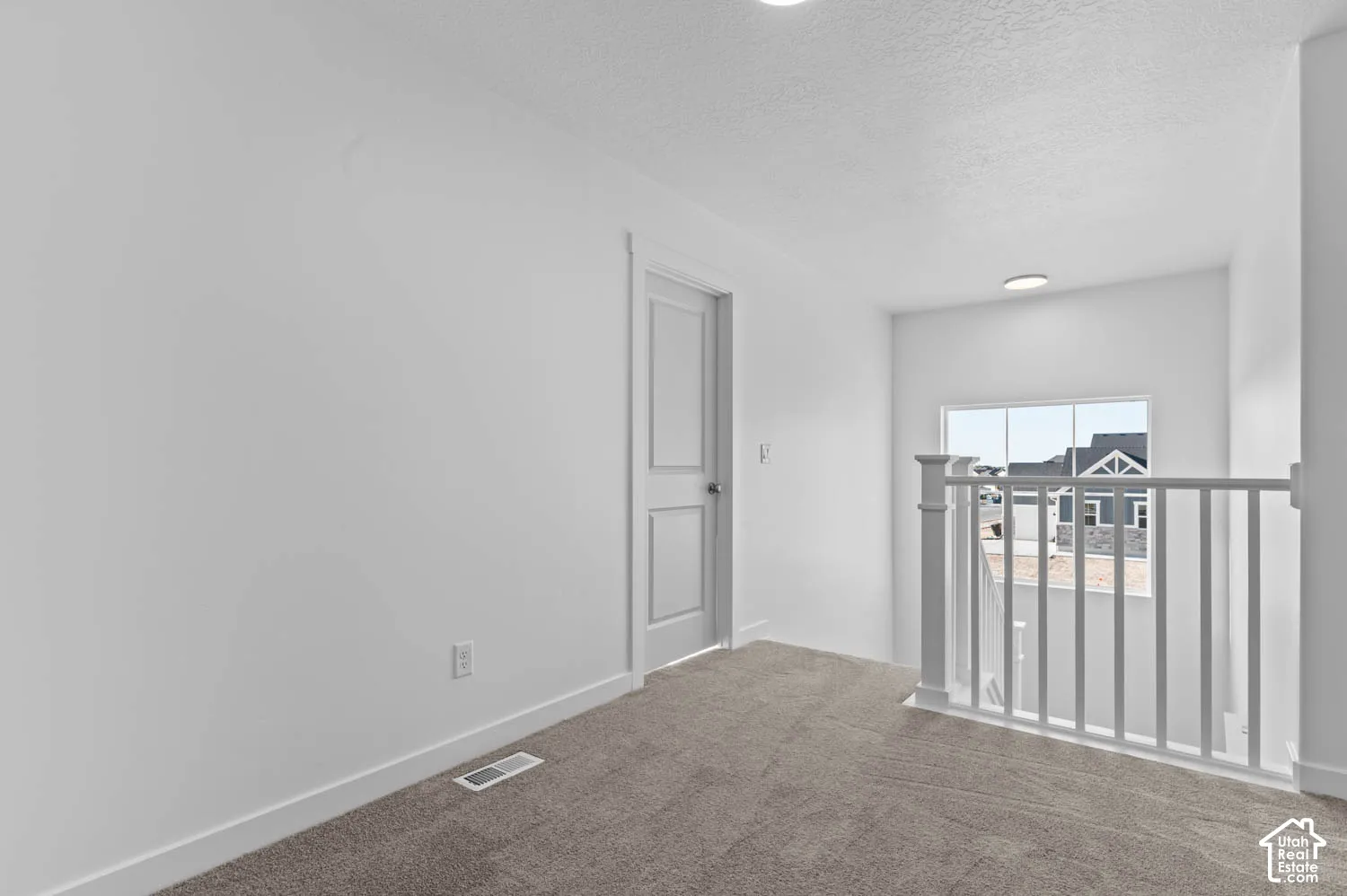 Carpeted landing featuring a white painted balustrade, a window with white trim, and a white paneled door