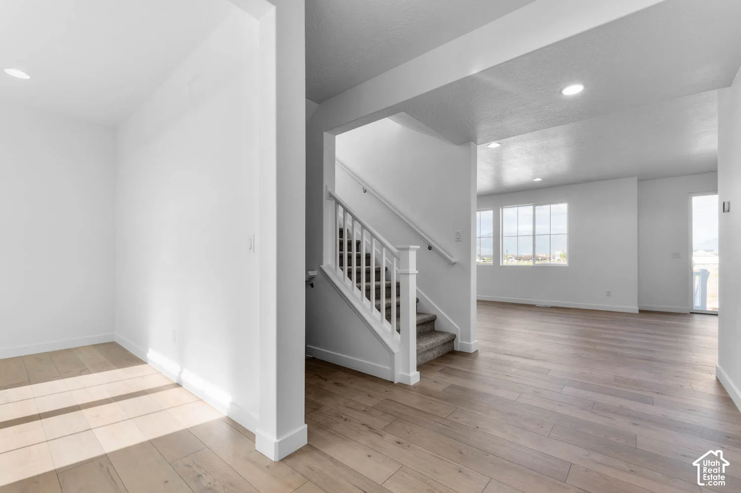 Wood-finish flooring, recessed lighting, white painted interior, staircase with carpeted treads and white wood railing, and multiple windows