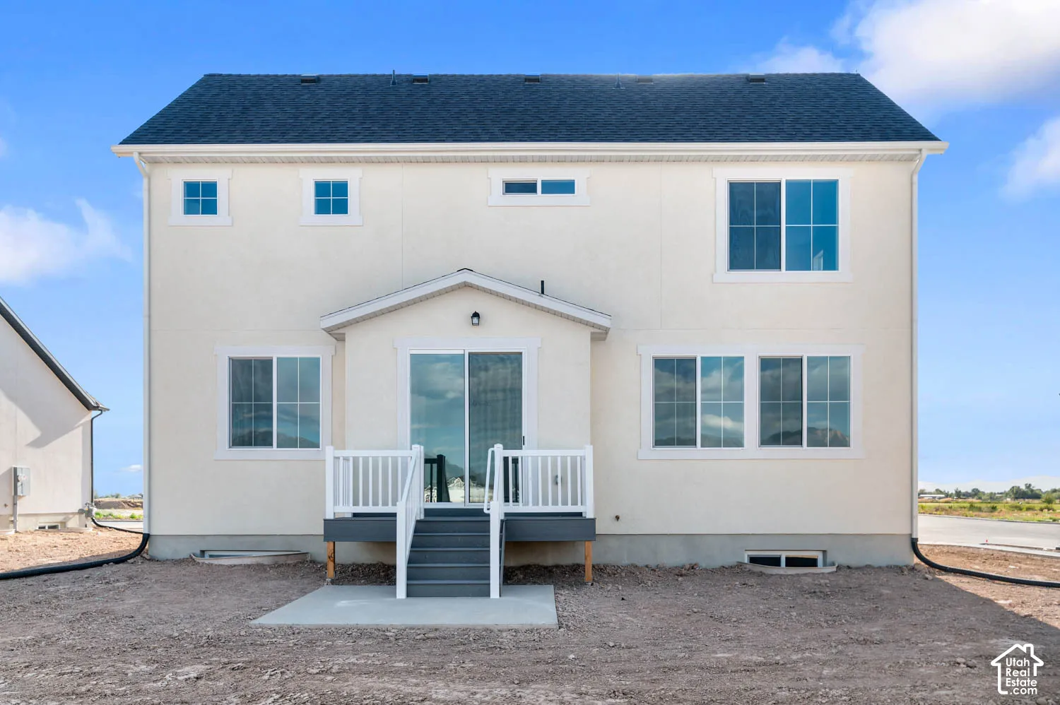 Rear exterior featuring a deck with white railings and gray steps, white stucco siding, and a dark shingle roof