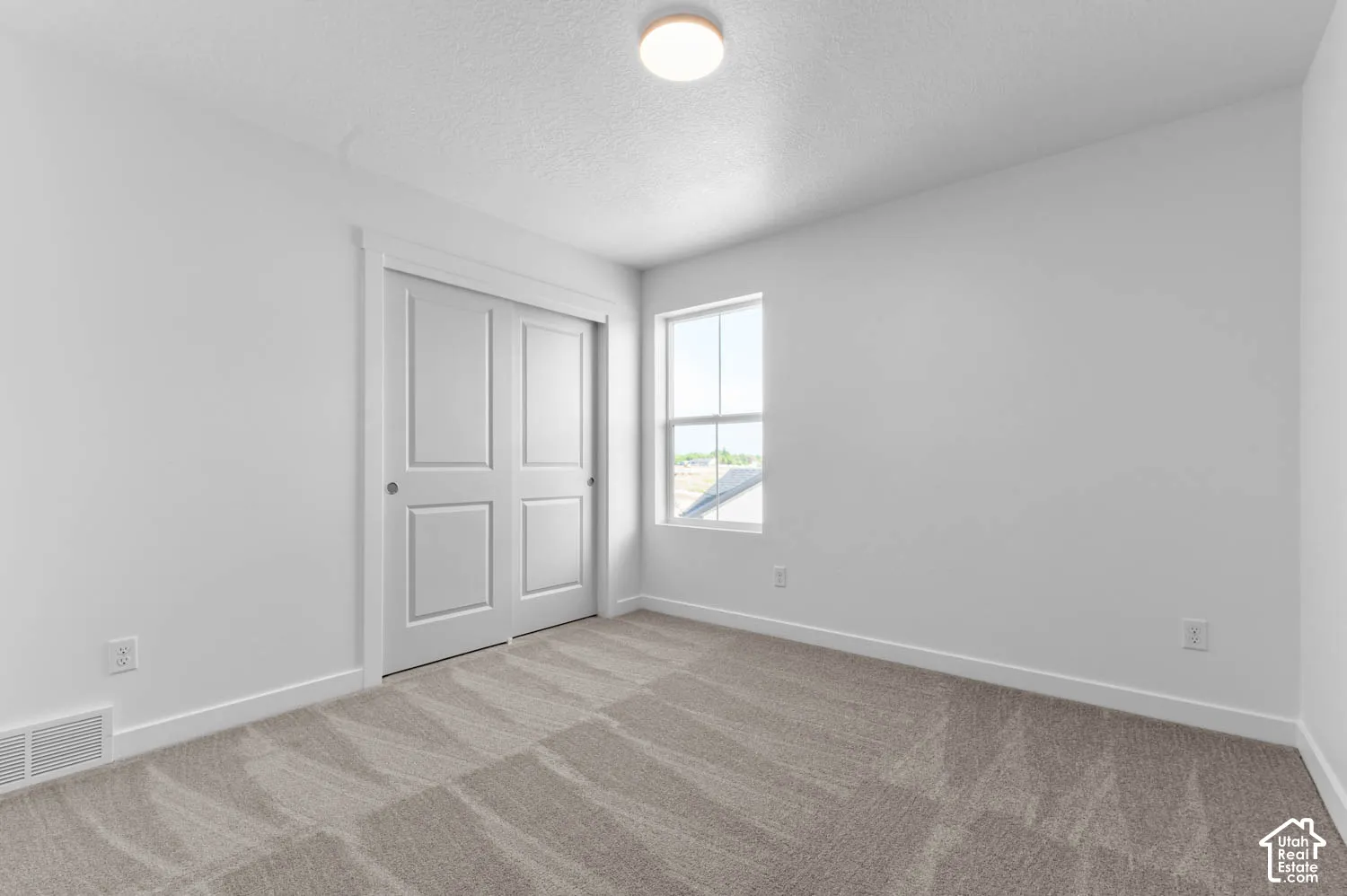 Sliding panel closet doors, neutral tone carpet, white window trim, and a flush mount ceiling light