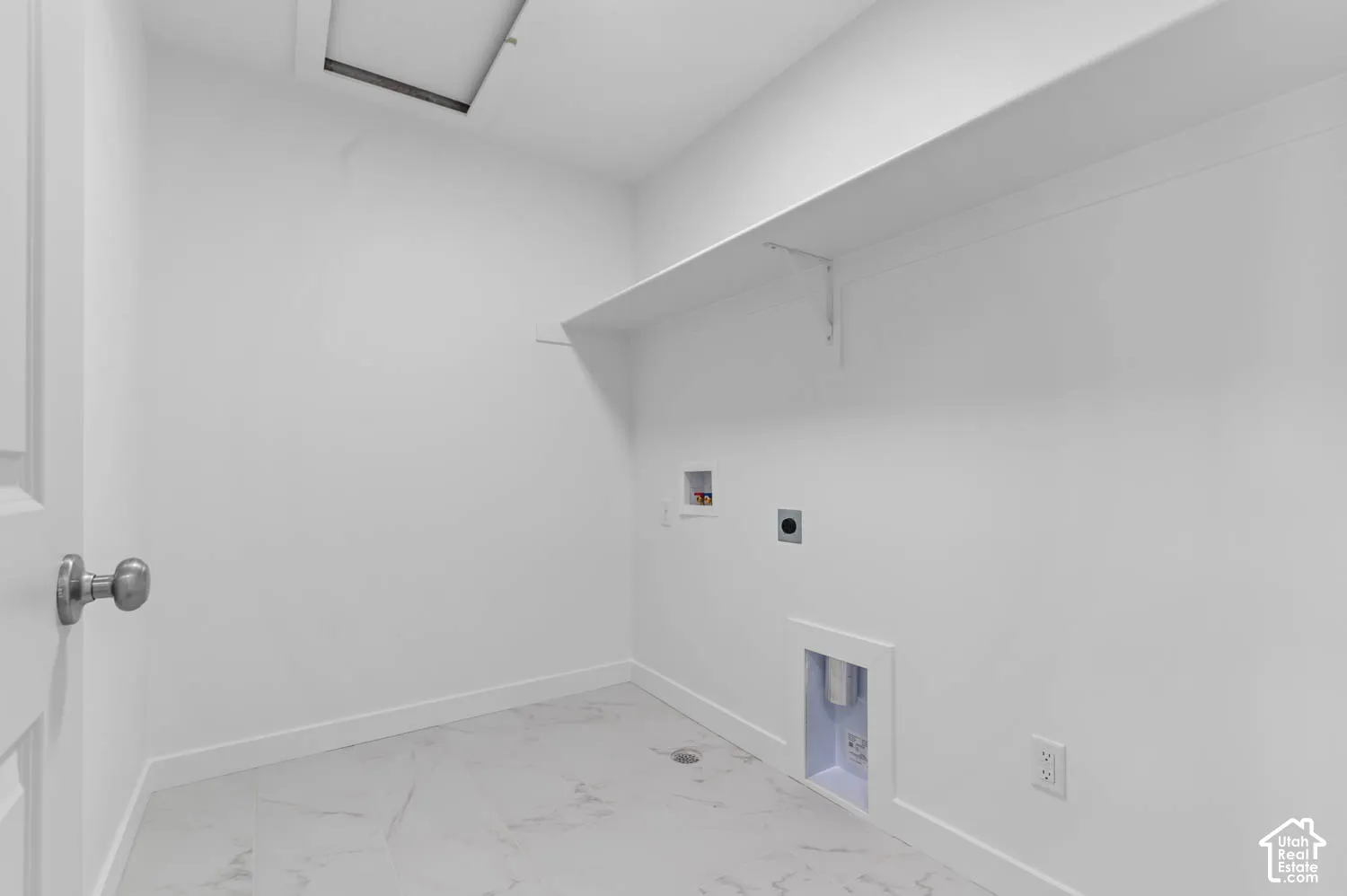 White interior walls with a single shelf, equipped with appliance hookups and a ceiling access panel