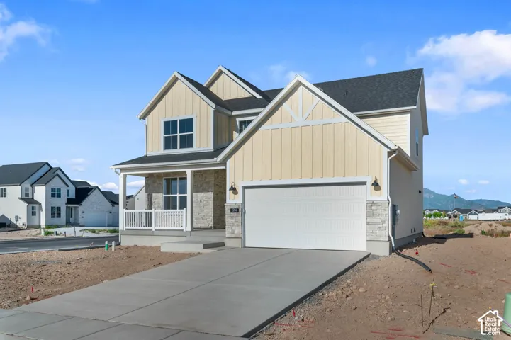 Exterior featuring board and batten siding, stone facade accents, covered front porch with white railing, attached two-car garage, and concrete driveway