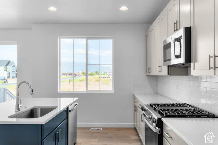 Kitchen featuring light-finish cabinetry, white subway tile backsplash, stainless steel appliances, and a central island with a sink and dark blue base cabinetry