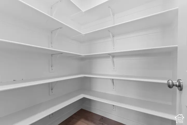 Corner pantry with multiple white shelves, wood-finish flooring, and a white door with a brushed nickel knob