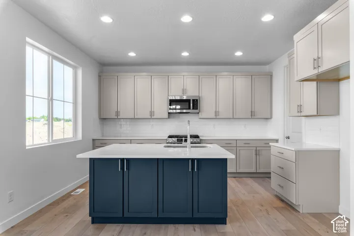 Kitchen featuring an island with a white countertop and blue cabinetry, wood-finish flooring, recessed lighting, and a window