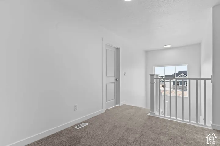 Carpeted landing featuring a white painted balustrade, a window with white trim, and a white paneled door