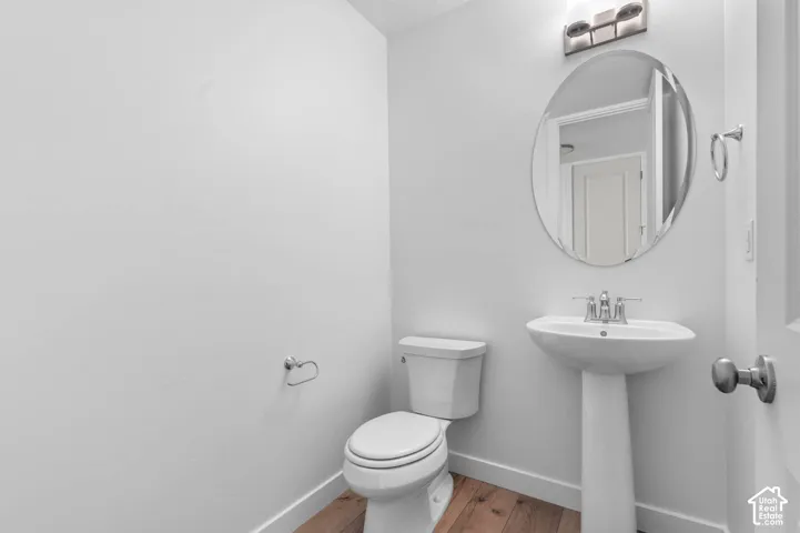Pedestal sink with chrome fixtures, oval mirror, wall-mounted light fixture, and wood-finish flooring
