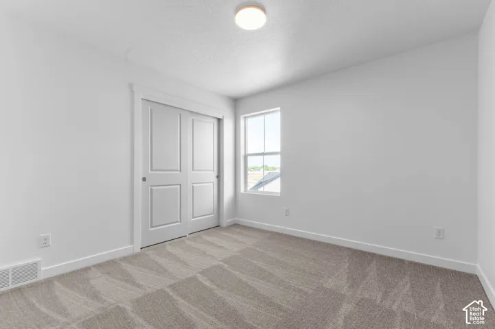Sliding panel closet doors, neutral tone carpet, white window trim, and a flush mount ceiling light