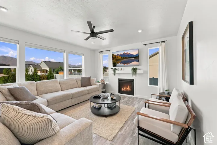 Spacious living area featuring abundant natural light, wood-finish flooring, a contemporary ceiling fan, and a built-in fireplace with a mantel