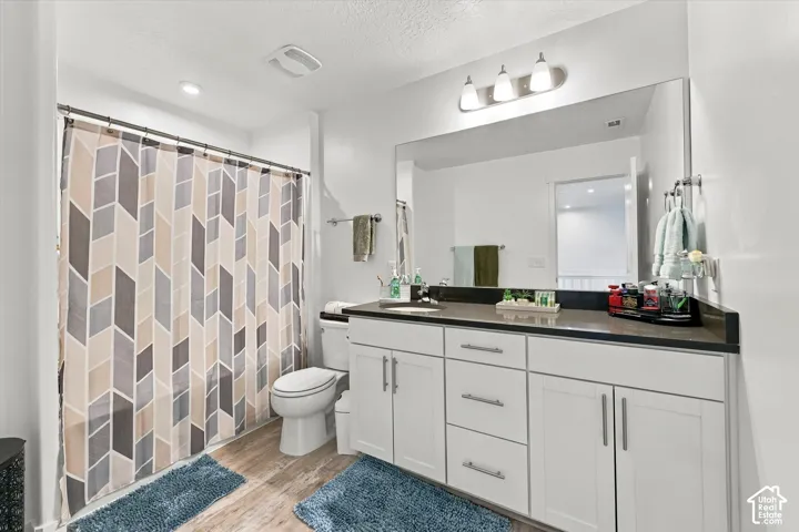 Double vanity with a dark countertop and white cabinetry, large wall-mounted mirror, wood-finish flooring, recessed lighting, and a built-in shower/tub combination